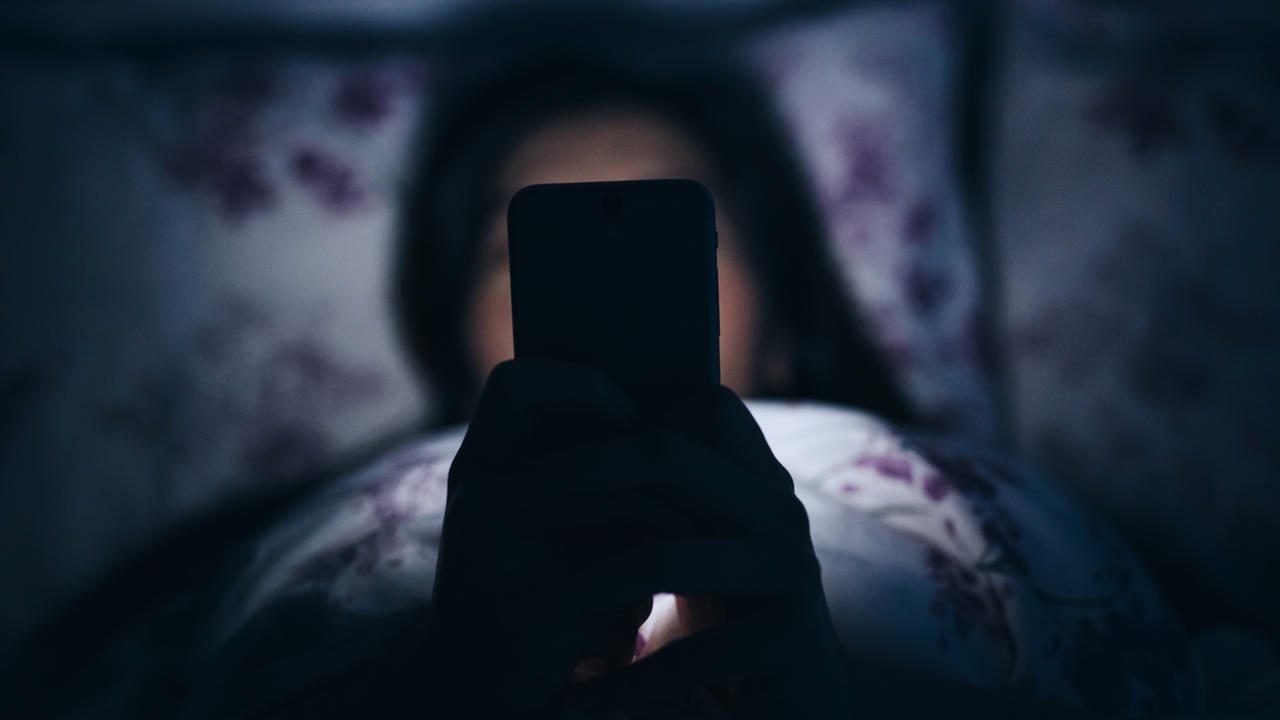 Woman reading and texting on smartphone in bed